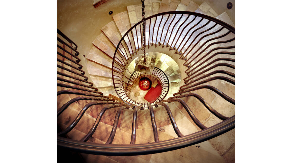 Spiral staircase in Tuscan-style home, looking down from top floor. Architecture and landscape architecture by NSPJ Architects.